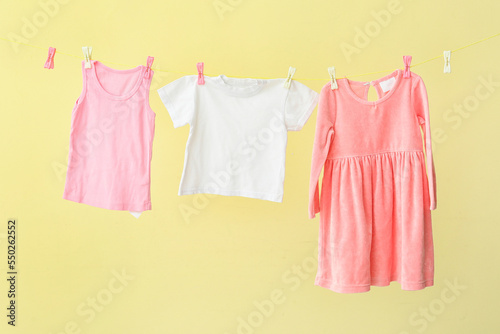 Different baby clothes hanging on rope against yellow background