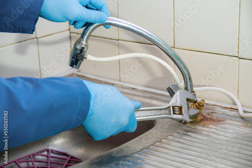 The plumber unscrews the old rusty faucet in the kitchen with a wrench. The master works in rubber protective gloves