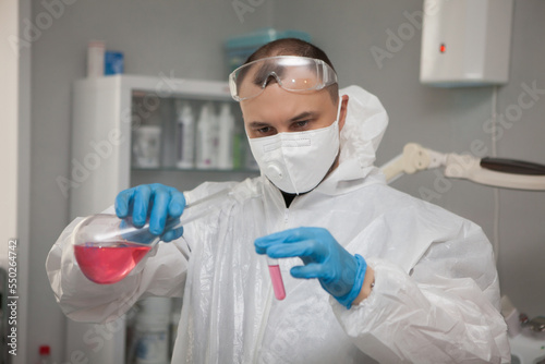 Scientific virologist. Biologist in protective suit and blue gloves holds test tube and flask. Test tube with viruses concept. Medicine and antidote in doctor hands. Virus University employee.