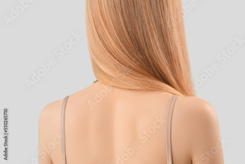 Back of woman with long blonde hair on light background