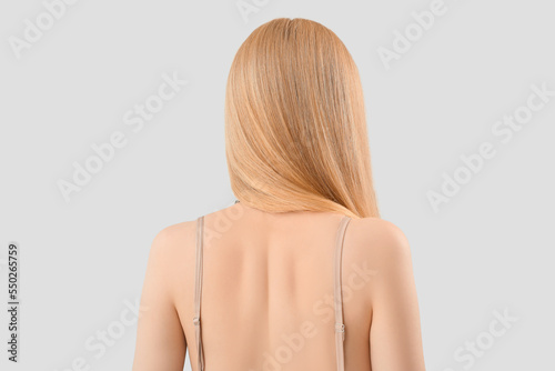 Back of woman with long blonde hair on light background