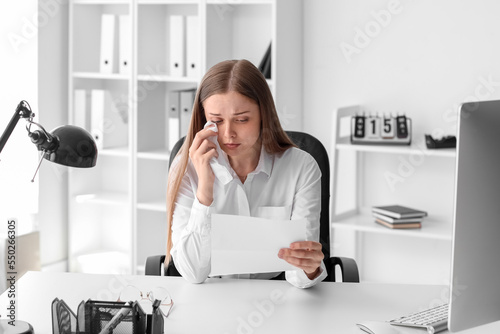 Young woman with order for her dismissal crying at table in office