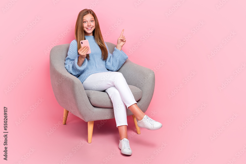 Full body photo of funky teenager schoolkid girl sit sofa relax smartphone finger direct copyspace follow media isolated on pink color background Full body photo of funky teenager schoolkid girl sit sofa relax smartphone finger direct copyspace follow media isolated on pink color background
