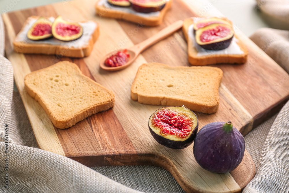 Wooden board of tasty bruschettas with cream cheese and fresh figs on table, closeup