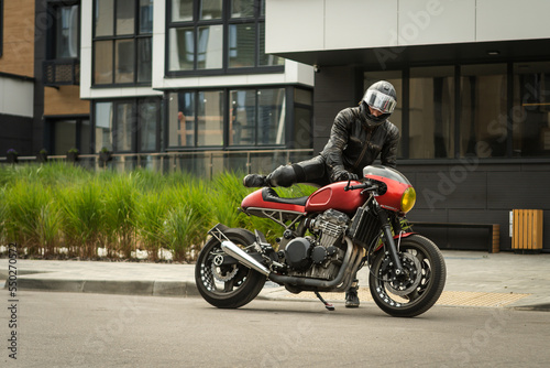 Biker in protective helmet sits on red motorcycle