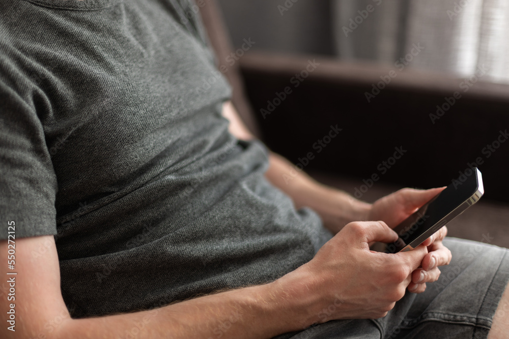 Man sitting on a couch with mobile phone in his hands. Relaxing at home.