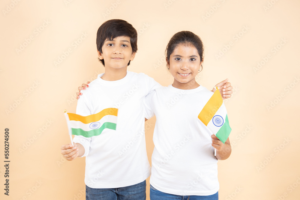 Cheerful indian little boy and girls kids wearing white t-shirt holding indian national flag isolated on beige background, happy independence day, 15th of august, republic day, Protestantism concept. Cheerful indian little boy and girls kids wearing white t-shirt holding indian national flag isolated on beige background, happy independence day, 15th of august, republic day, Protestantism concept.