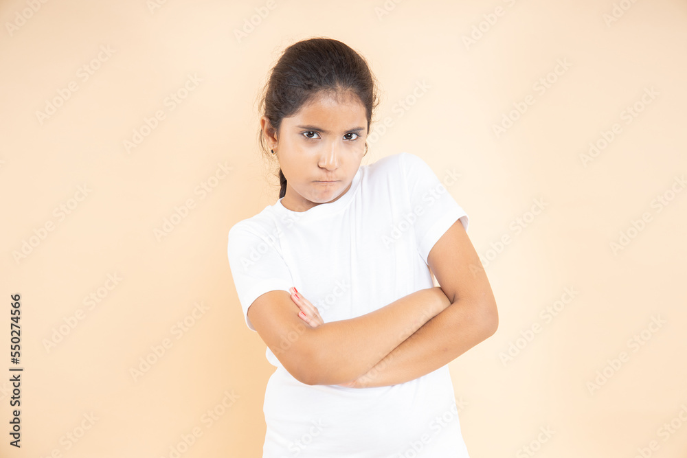 Portrait of angry Indian girl standing with folded arms looking at camera isolated over beige studio background. Asian female kid annoyed hands crossed posing , feeling dissatisfied Portrait of angry Indian girl standing with folded arms looking at camera isolated over beige studio background. Asian female kid annoyed hands crossed posing , feeling dissatisfied
