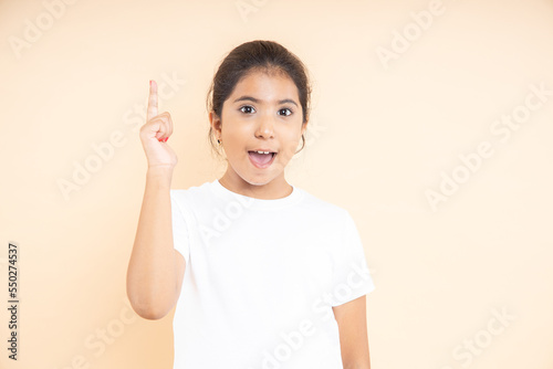 Smart little Indian girl wearing plane white t-shirt having an idea expression with smile on his face found a solution isolated on beige studio background.