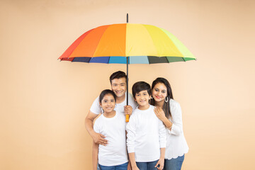 Happy indian family standing under big colorful umbrella against beige background. parents and children. Life and health insurance Safety concept. Togetherness, summer season. 