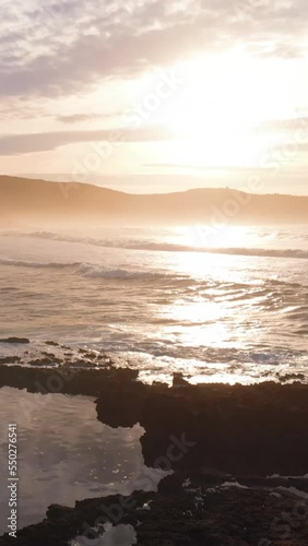 plane moving from drone on a rocky beach at sunset with haze and foam in the water. Vertical video for smart phone