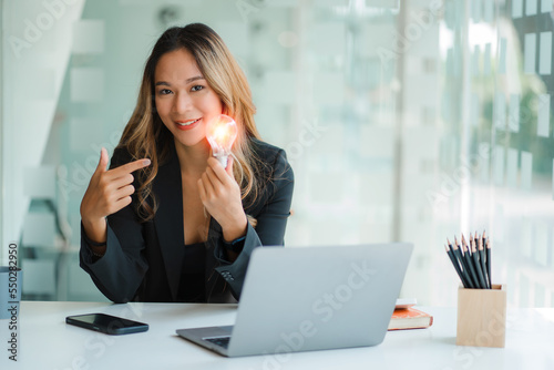 Businesswoman holding a light bulb. Innovation concept with technology  innovation and creativity  energy saving presentation concept. Young woman hand holding light bulb while working on laptop