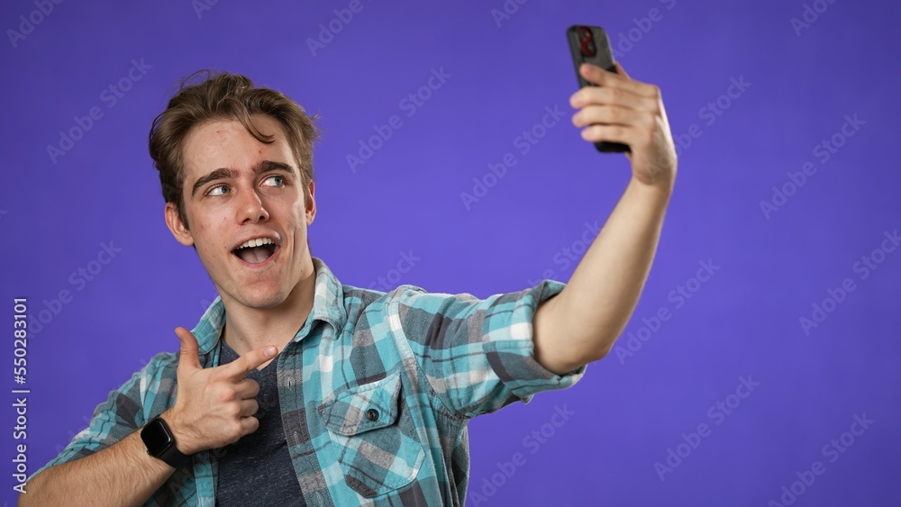 Portrait of happy smiling young guy 20s taking selfie with mobile cell phone conducting pleasant conversation isolated on purple background studio. Portrait of happy smiling young guy 20s taking selfie with mobile cell phone conducting pleasant conversation isolated on purple background studio.