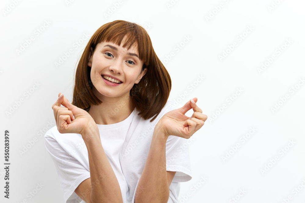 a happy, sweet, inspired red-haired woman stands on a white background in a white T-shirt and, smiling pleasantly at the camera, shows a heart in Asian style with her fingers a happy, sweet, inspired red-haired woman stands on a white background in a white T-shirt and, smiling pleasantly at the camera, shows a heart in Asian style with her fingers