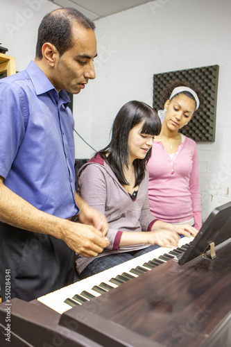 Music Students: Piano Accompanist. A teacher helping a young keyboard player and singer find the right note. From a series of related images.