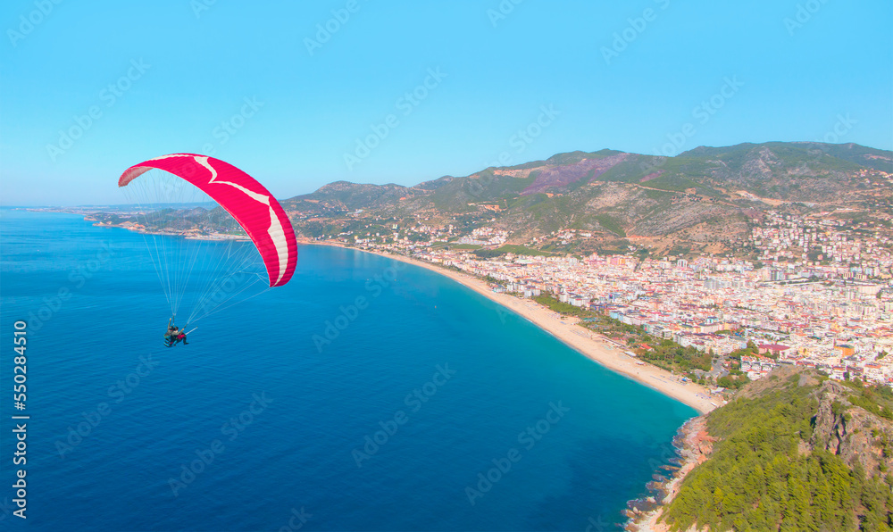 Naklejka premium Paraglider flies in the sky, Famous Cleopatra Beach in the background - Alanya, Turkey