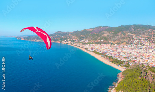 Paraglider flies in the sky, Famous Cleopatra Beach in the background - Alanya, Turkey