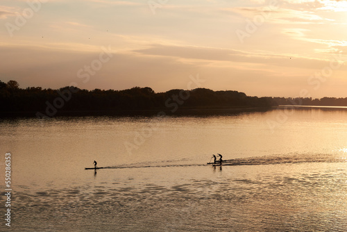 River landscape with silhouettes of people paddle on stand up paddle boards  SUP  at calm surface of evening  autumn Danube river