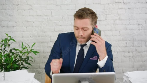 An overworked businessman in an office is stressed and frantic with his busy workload and is under preassure whilst talking on the phone