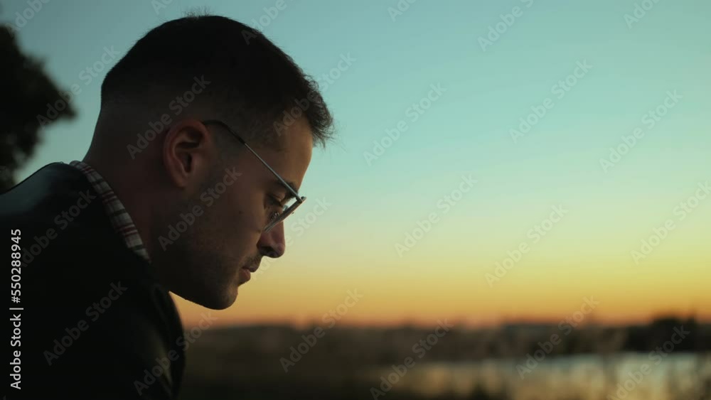 Slow motion of a generation Z millennial traveler or travel blogger wearing glasses, immersed in taking photos for social media by flying his drone using a remote controller and a smartphone at sunset