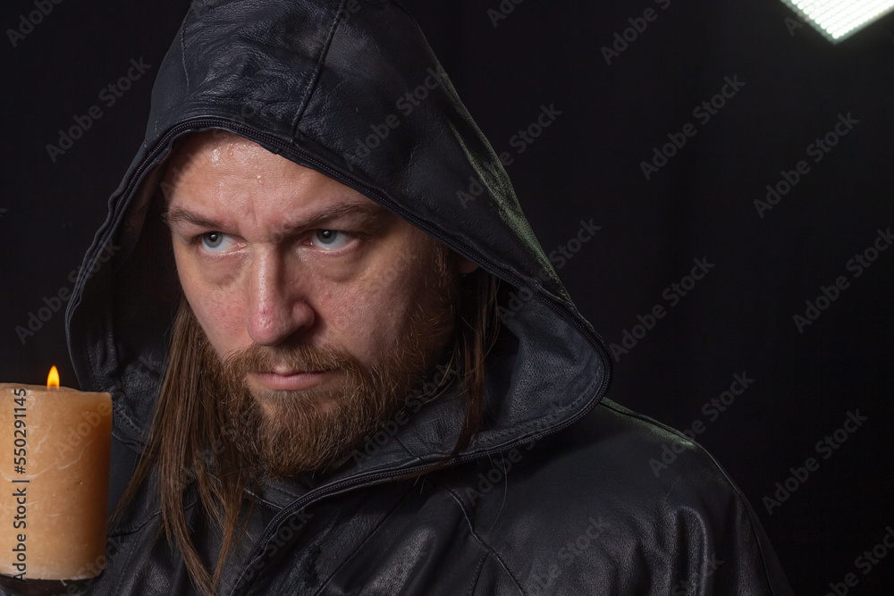 Portrait of a man in a cloak with a hood against a dark background with a candle on candlestick Portrait of a man in a cloak with a hood against a dark background with a candle on candlestick