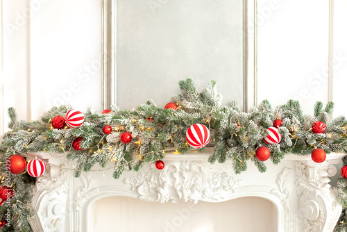 Xmas tree with colorful festive decorations on the fireplace. Christmas decorations for fireplace at home. Spruce branches, toys and red balls on white fireplace. New Year.	