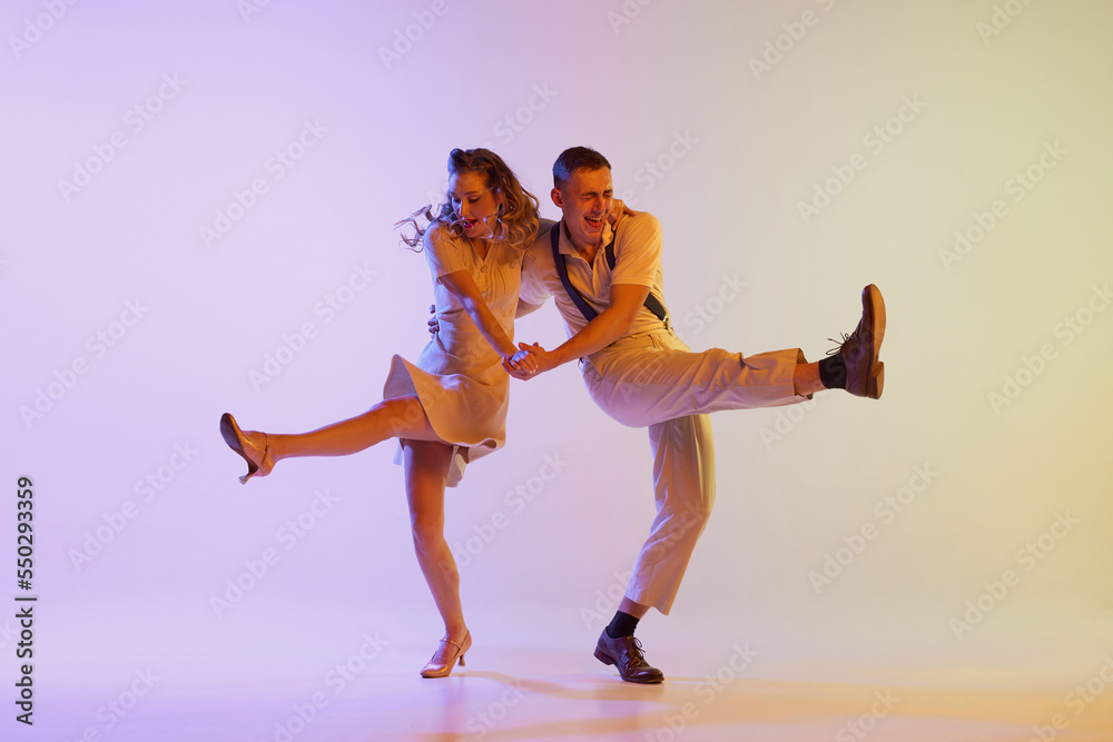 Beautiful girl and man in retro style costumes dancing incendiary dances isolated on gradient lilac color background in neon light. Concept of art, 60s, 70s culture