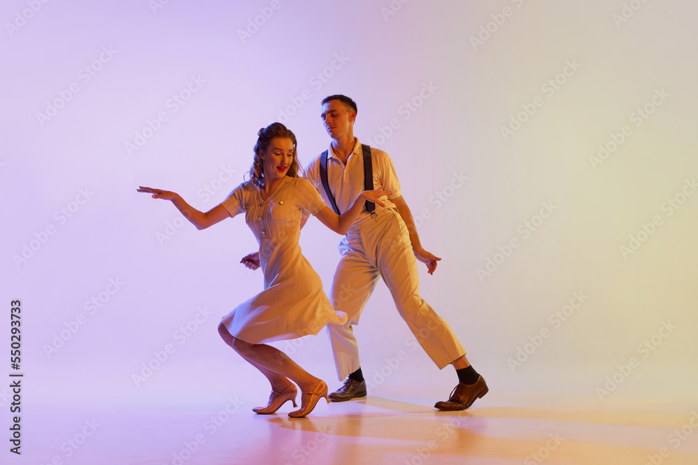 Incendiary dance. Emotional couple of dancers in retro style outfits dancing social dances isolated on gradient lilac color background in neon light. Concept of art, 60s, 70s culture