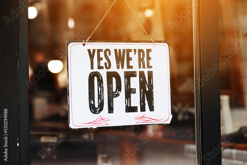 Inscription Yes we're open metal plate with black and white sign on glass door store, cafe, beautystore, barbershop after coronavirus lockdown quarantine. business reopen again