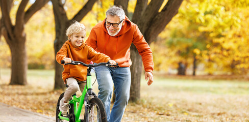 Happy family grandfather teaches child grandson  to ride a bike in park