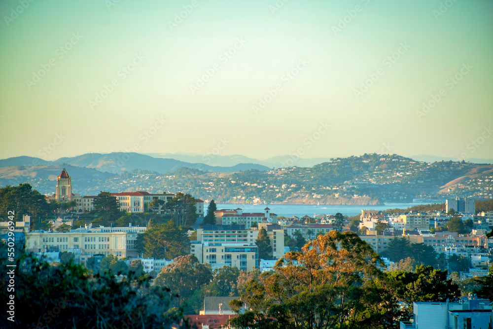 Sprawling buildings with background moutains and lakes with visible ocean and orange and blue gradient sunset sky in afternoon