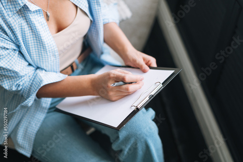 Crop photo of young woman in bue shirt with notes in hands sitting on chair in room