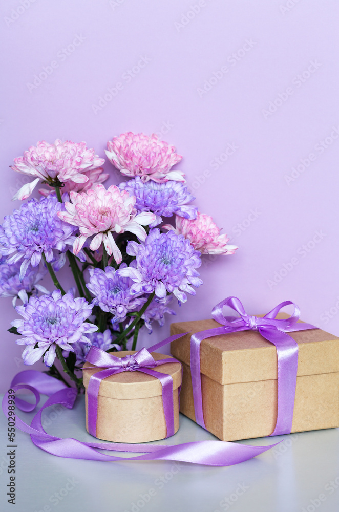 Romantic congratulations to a loved one on birthday, women's day on March 8 or Mother's day. Bouquet of delicate chrysanthemums and two gifts in boxes with purple ribbons on pastel pink background