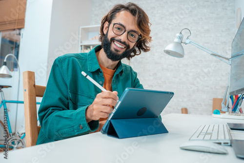 Young designer looking at camera while working with graphics tablet and laptop. High quality photo