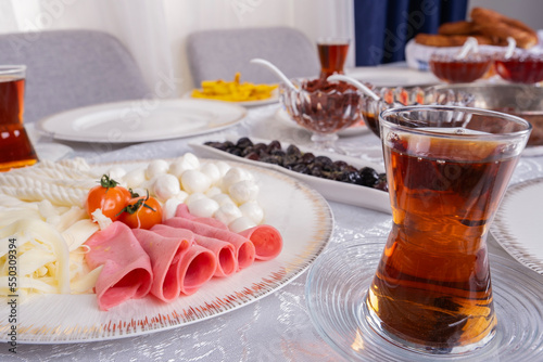 Turkish tea, close up photo glass of fresh hot Turkish tea. Modern breakfast table. Sunday morning family routine. Knit, String and ball of cheese with ham in plate. Ready for eating.