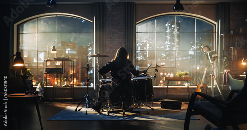 Person Sitting with Their Back to Camera, Playing Drums During Rehearsal in a Loft Studio with Sunlight. Drummer Practising Alone Before a Live Concert on Stage. Evening or Night Session.