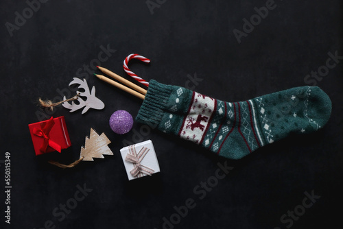 Christmas stocking filled with decorations, small presents, sweets and toys. Dark background, top view.