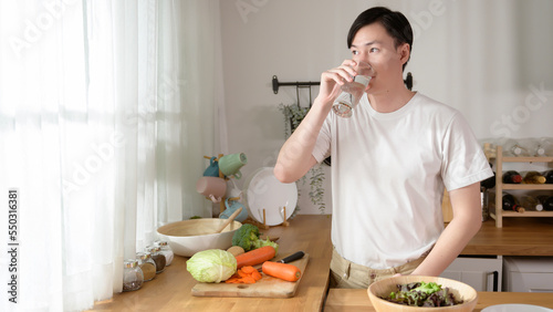 An Asian young man drinking fresh water in kitchen at home   healthy lifestyle concept