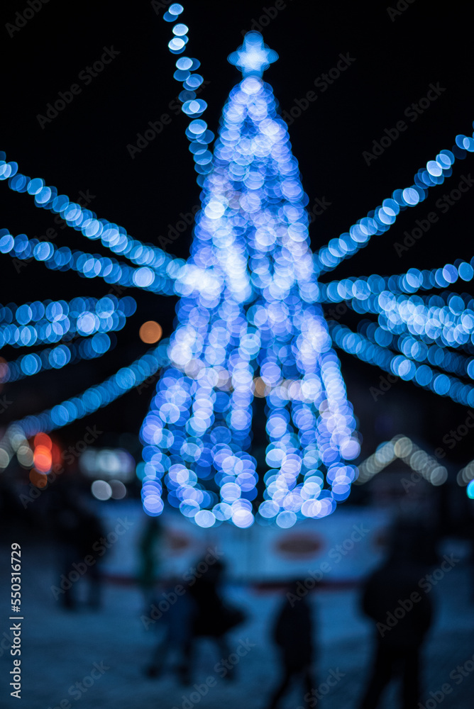 Bokeh silhouette of Christmas tree. Christmas tree with decorations and lights bokeh in a black background, outdoor