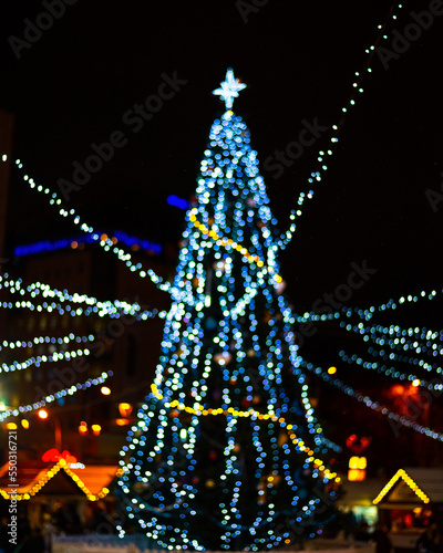 Bokeh silhouette of Christmas tree. Christmas tree with decorations and lights bokeh in a black background, outdoor