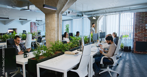 People IT developers sitting at computers and working. Support office employees. Man coming and helping in work to colleague. Male and female talking and discussing. Team of startuppers.