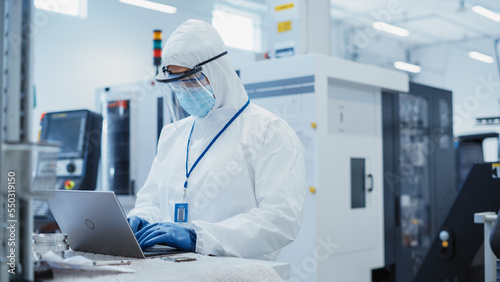 Modern Technology Concept: Engineer in Coverall Working on Laptop Computer, Examining a Circuit Board with Microchips and Typing Data. Technician Testing New Electrical Equipment.