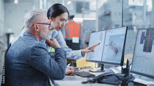 Factory Office Facility: Industrial Engineers Drafting Blueprints of a Heavy Industry Machine Parts on a Computer CAD Software. Asian Female Technician Discusses Work with Middle Aged Designer.