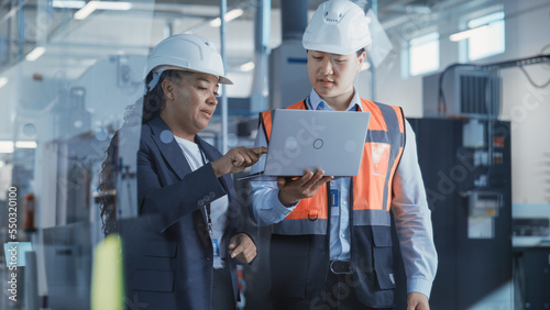 Fotografía Two Professional Heavy Industry Engineers Wearing Safety Uniform and Hard Hats Discussing Factory Work on Laptop Computer