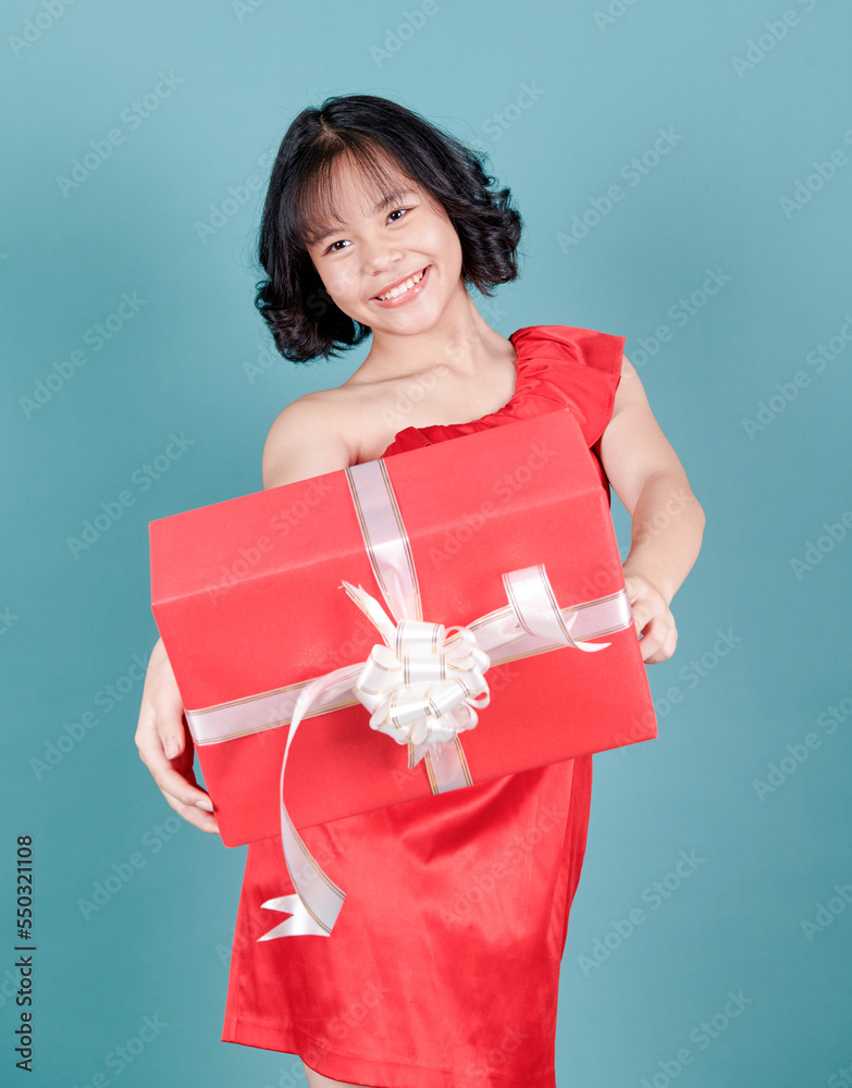 Happy pretty young asian woman holding gift box over blue isolated background. Holidays, celebration asia girl in red dress. Portrait of happy charismatic girl shaking gift box Happy pretty young asian woman holding gift box over blue isolated background. Holidays, celebration asia girl in red dress. Portrait of happy charismatic girl shaking gift box