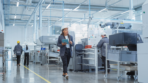Portrait of a Black Female Engineer in Hard Hat Walking and Using Laptop Computer at Electronic Manufacturing Factory. Technician Working on Daily Tasks and Research and Development Data.