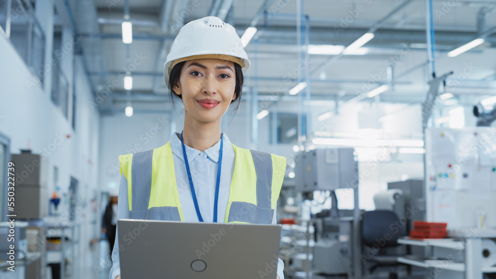 Portrait of a Happy and Smiling Asian Female Engineer in White Hard Hat Standing with Laptop Computer at Electronic Manufacturing Factory. Successful Employee Posing for Camera. Portrait of a Happy and Smiling Asian Female Engineer in White Hard Hat Standing with Laptop Computer at Electronic Manufacturing Factory. Successful Employee Posing for Camera.