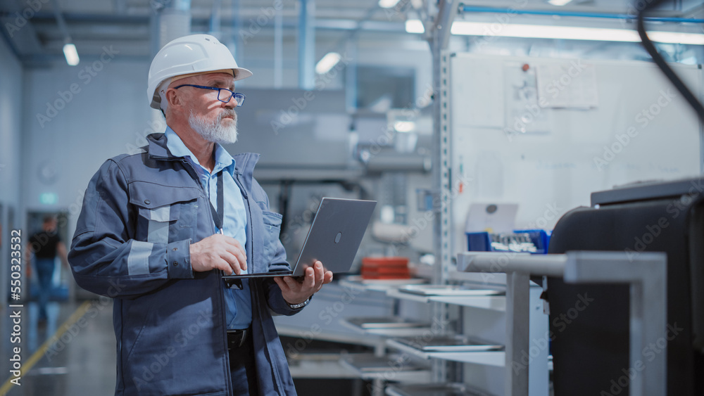 Bearded Middle Aged Chief Engineer Walking in a Factory Facility, Wearing a Work Suit, Stylish Blue Glasses and a White Hard Hat. Heavy Industry Specialist Working on Laptop Computer. Bearded Middle Aged Chief Engineer Walking in a Factory Facility, Wearing a Work Suit, Stylish Blue Glasses and a White Hard Hat. Heavy Industry Specialist Working on Laptop Computer.