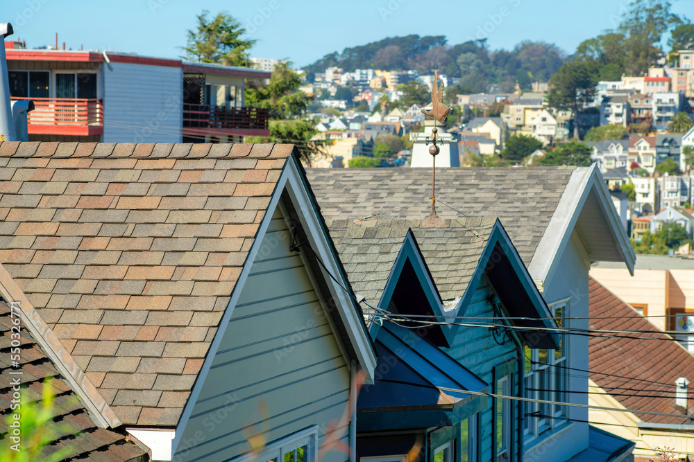 Rows of lit up roofs with brown tiles and double gable edges with deep suburban neighborhood background with front yard trees Rows of lit up roofs with brown tiles and double gable edges with deep suburban neighborhood background with front yard trees