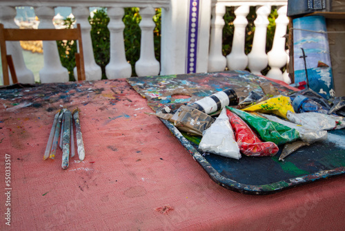 Pinturas y pinceles de un artista callejero trabajando por la voluntad en medio de la plaza de Benidorm con todas sus cosas puestas sobre un mantel con manchas. photo